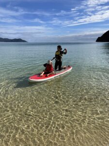 Woman and small child sitting on a paddle board in the Awaroa Bay