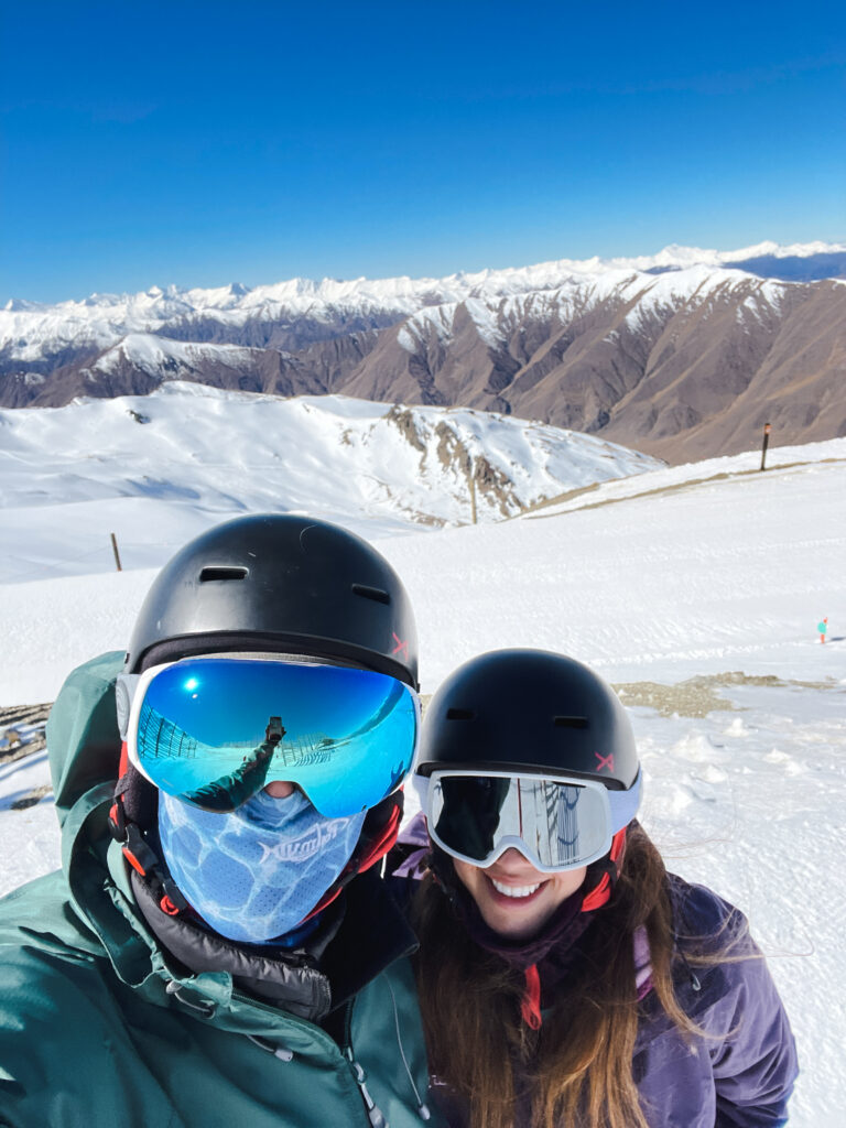 man and woman smiling while skiing in New Zealand with snow covered mountains in the background