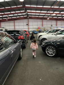 Two small children walking through the isles of a used car lot