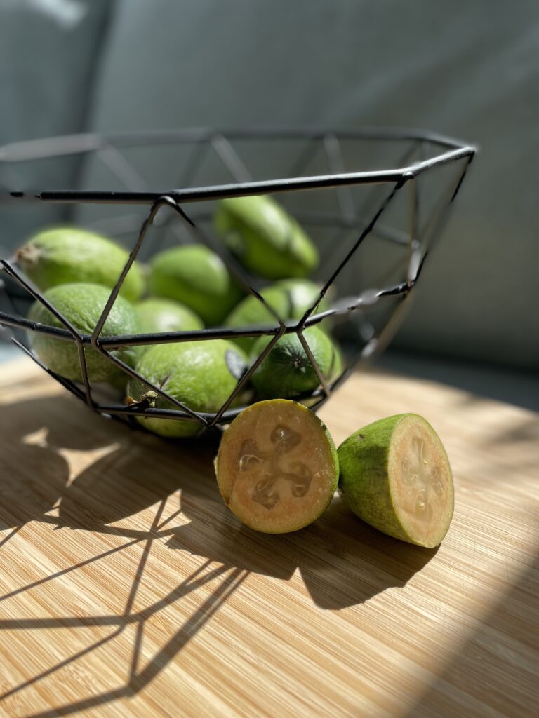 Basket of green feijoa fruit and one cut feijoa fruit 
