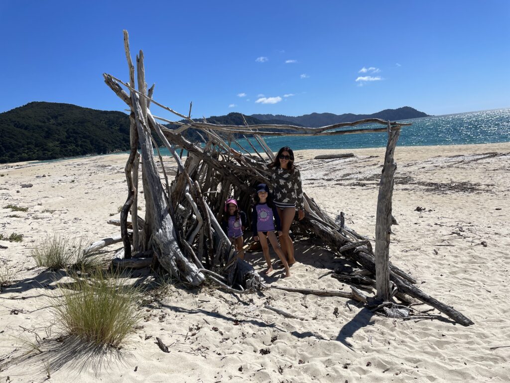 woman and two small girls standing beside a tent made of sticks at Awaroa Bay Beach