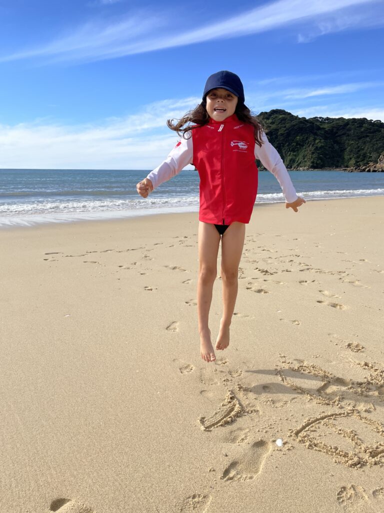 small girl jumping at awaroa bay beach