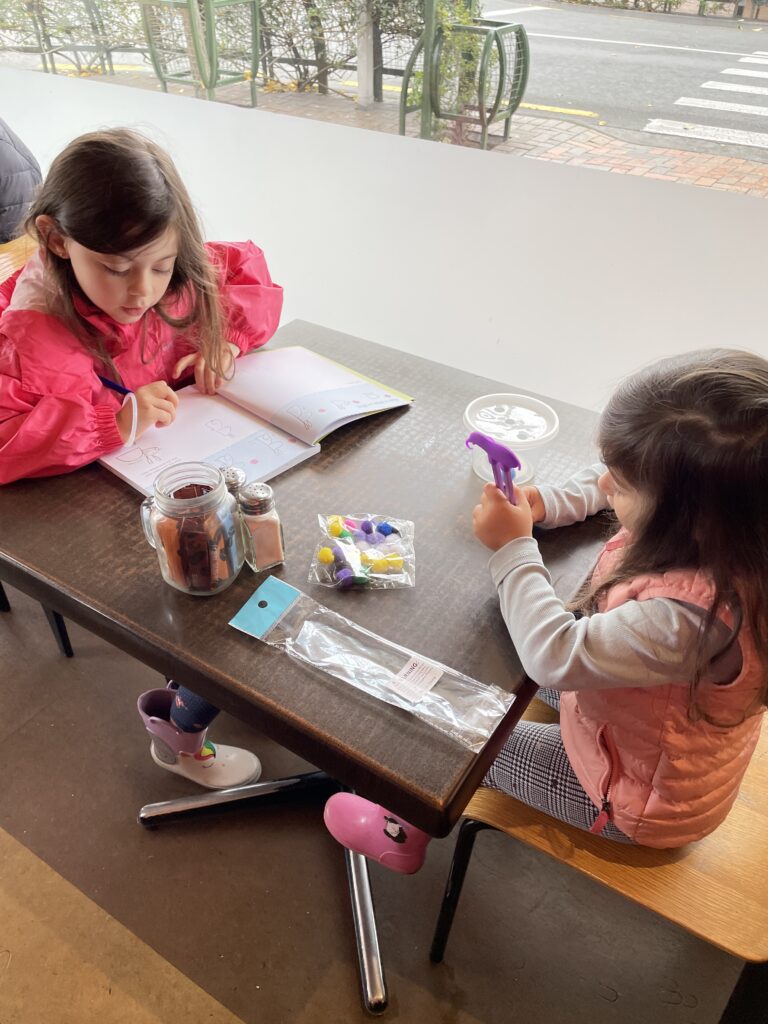 two little girls sitting in restaurant in New Zealand playing with Mini Voyager custom travel kit