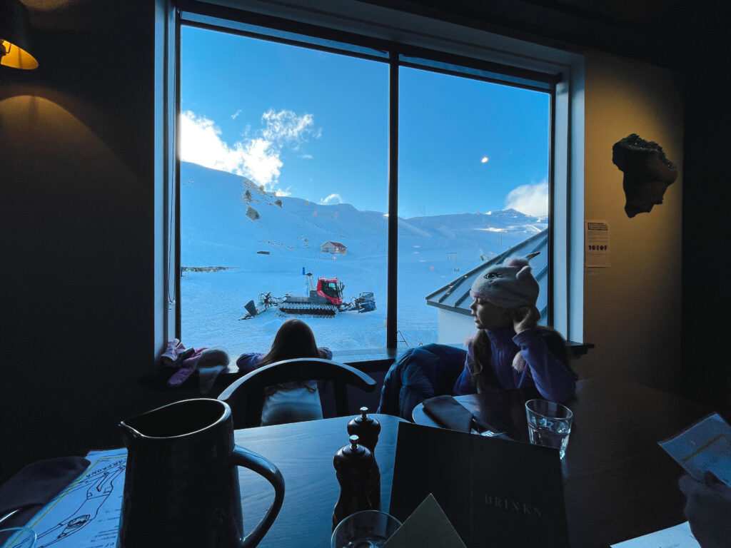 two little girls looking out at the snow covered mountain while sitting in restaurant I the Cardrona Alpine Resort